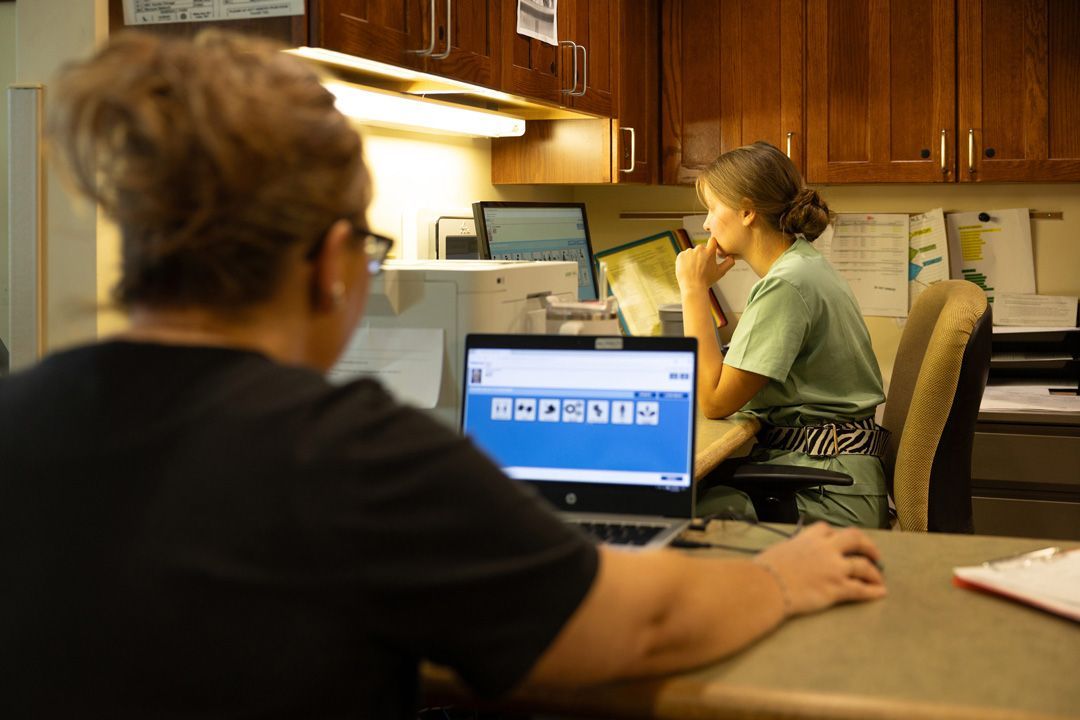 A woman is sitting at a desk in front of a laptop computer.