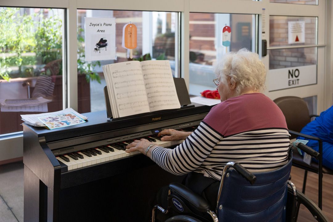An elderly woman in a wheelchair is playing a piano.