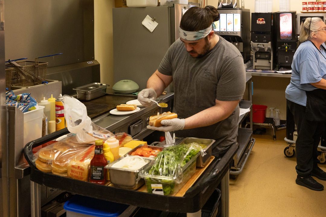 A man is preparing a hot dog in a kitchen