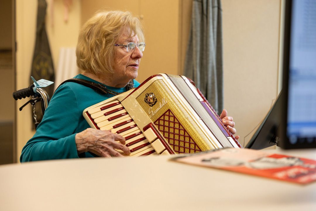 An elderly woman is sitting at a table playing an accordion.