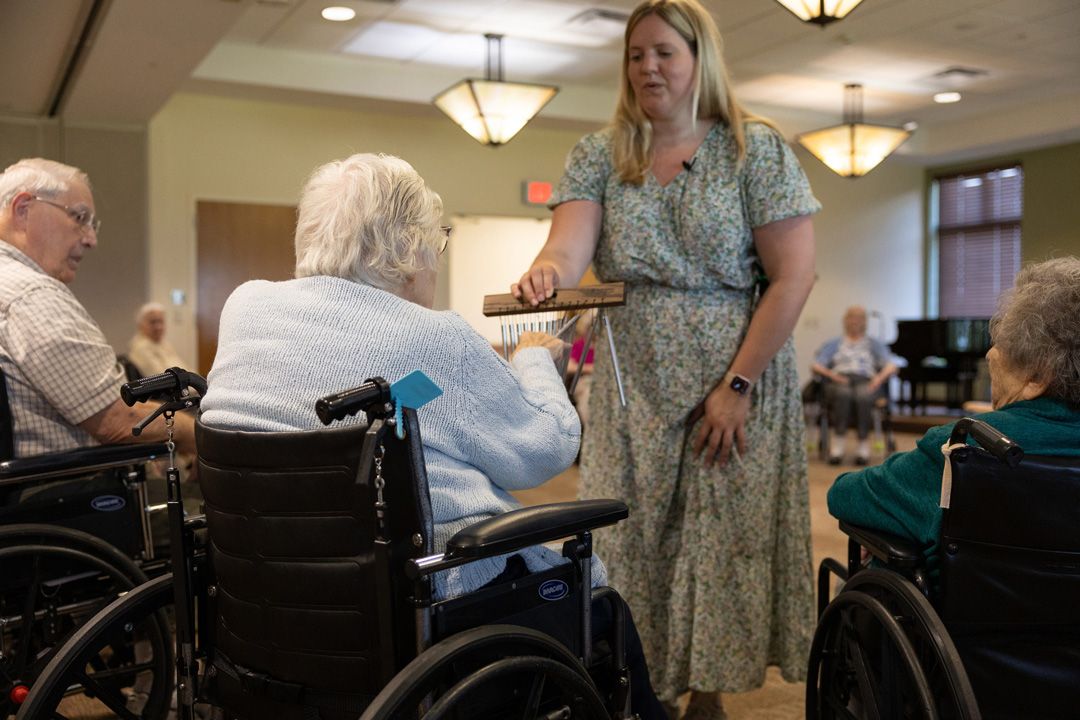 A woman is standing in front of a group of elderly people in wheelchairs.