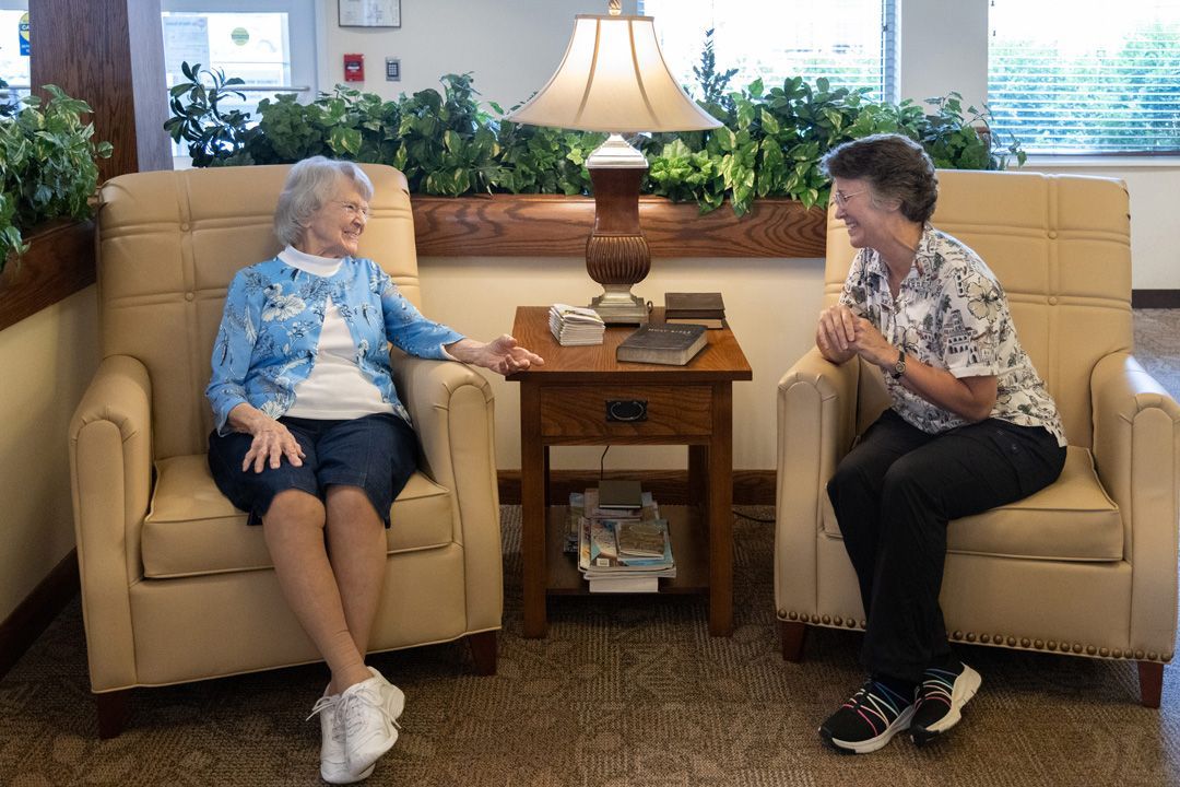 Two women are sitting in chairs in a living room talking to each other.