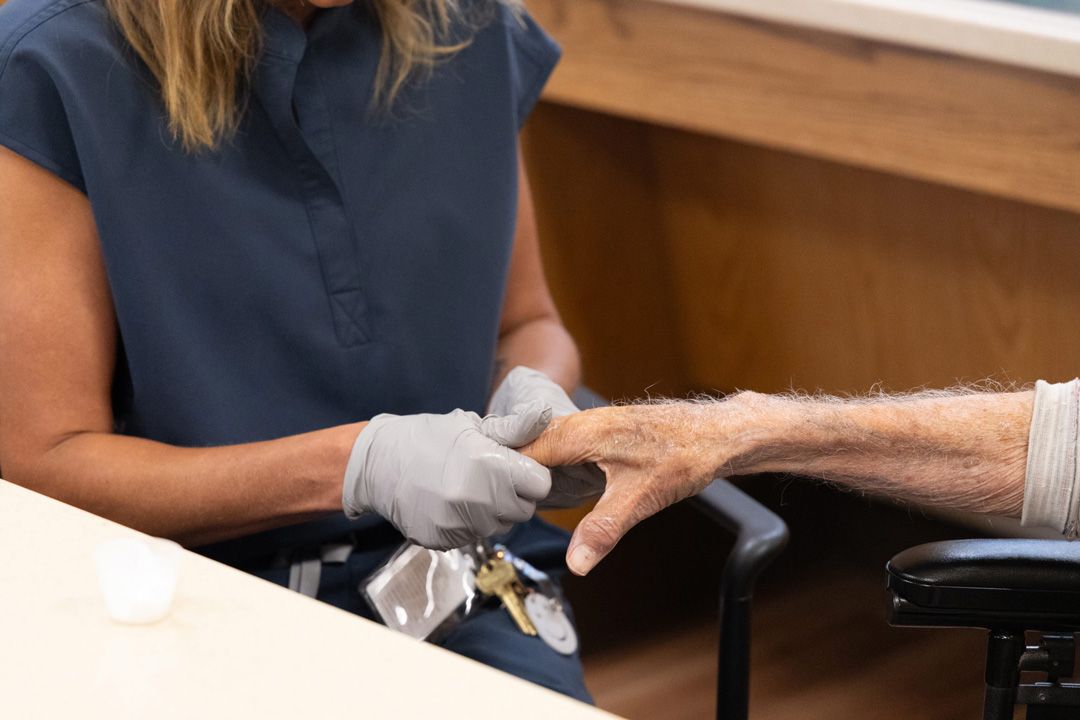 A woman is examining a man 's hand in a wheelchair.