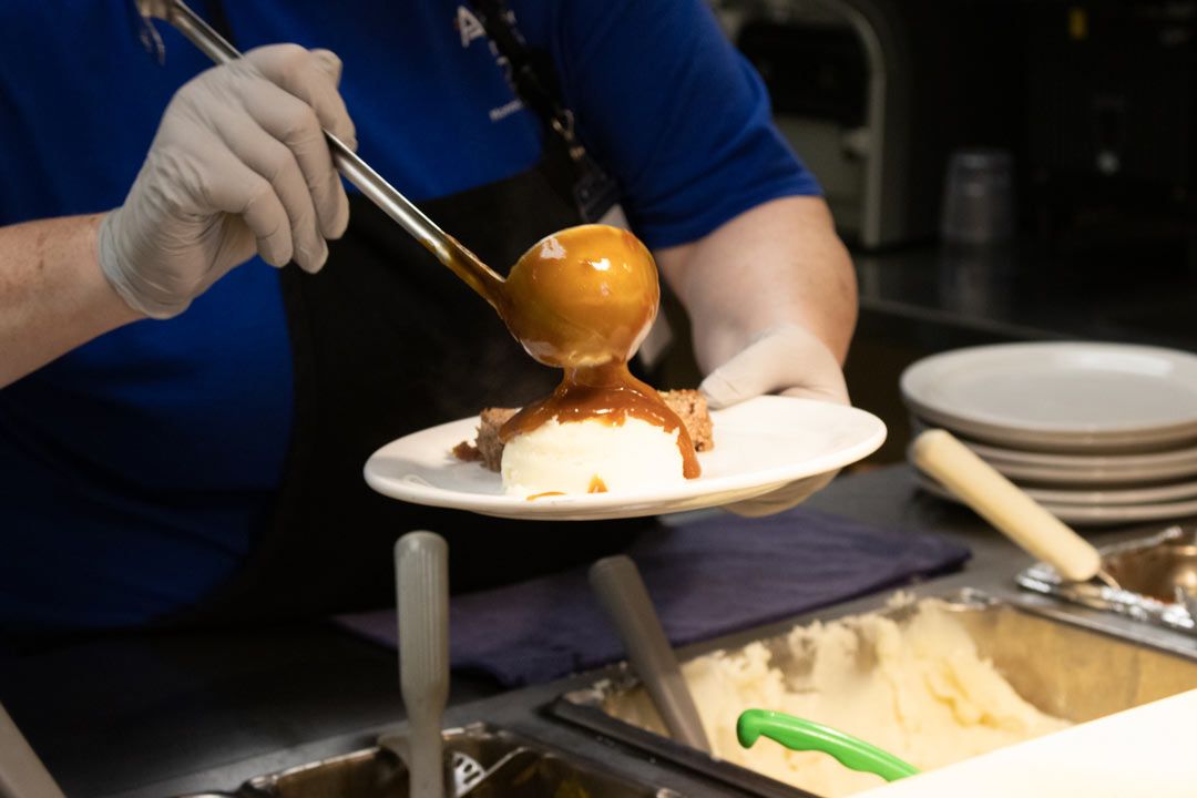 A person is pouring gravy on a plate of food.