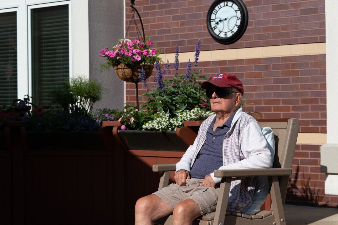 An elderly man is sitting in a chair in front of a clock.