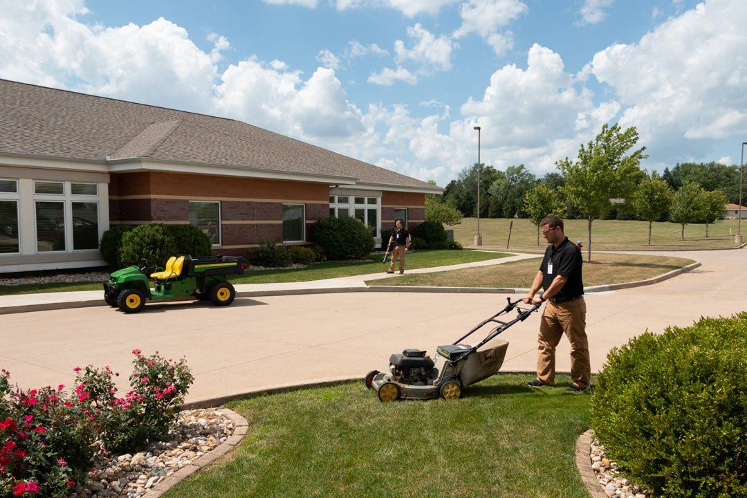 A man is mowing the grass in front of a building.