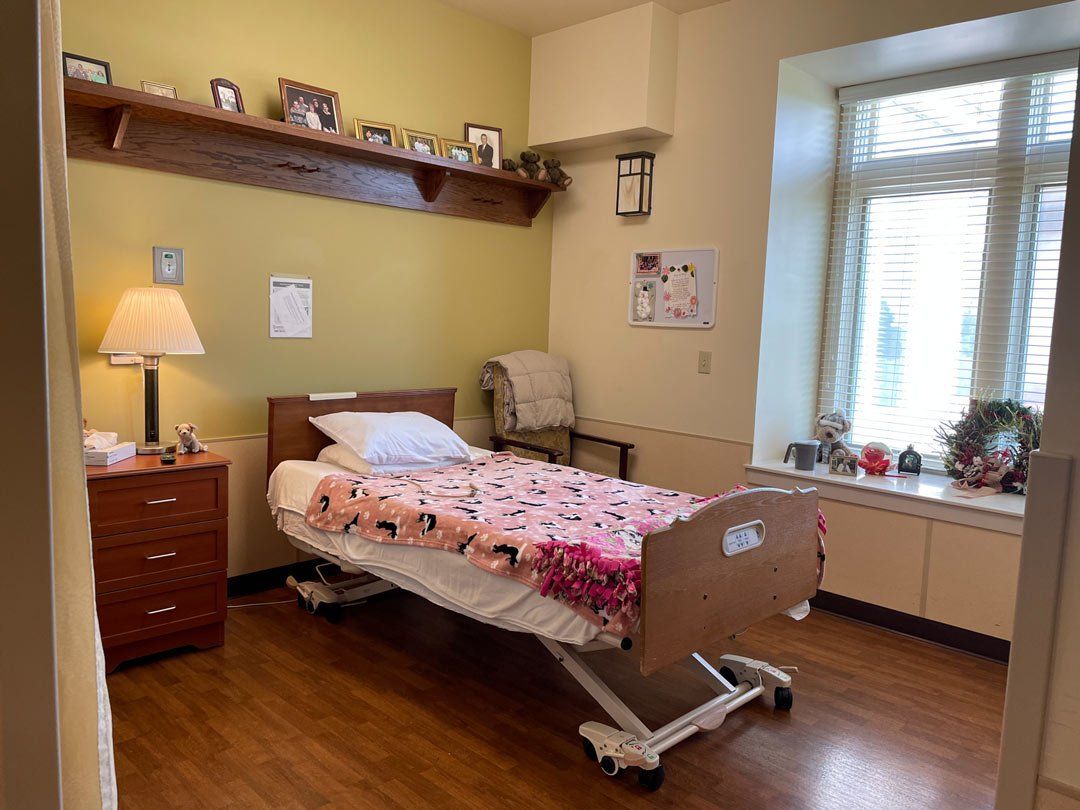 A hospital room with a bed , nightstand , lamp and window.