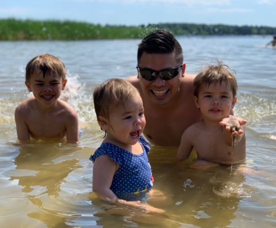 A man, Danny Truong, and three children are swimming in a lake.