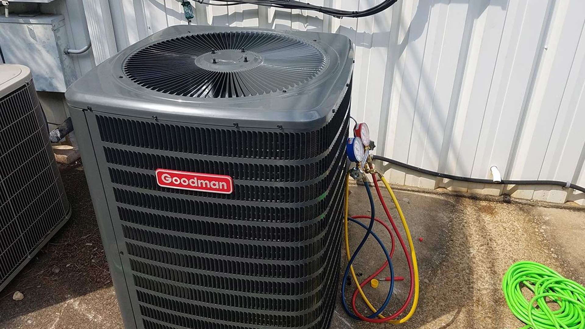 A large air conditioner is sitting on the ground next to a green hose.