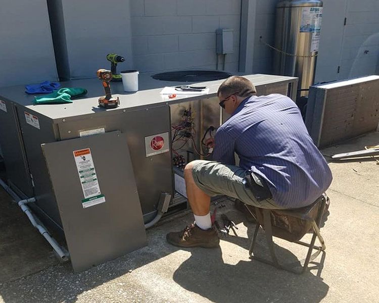 A man is kneeling down and working on an air conditioner.