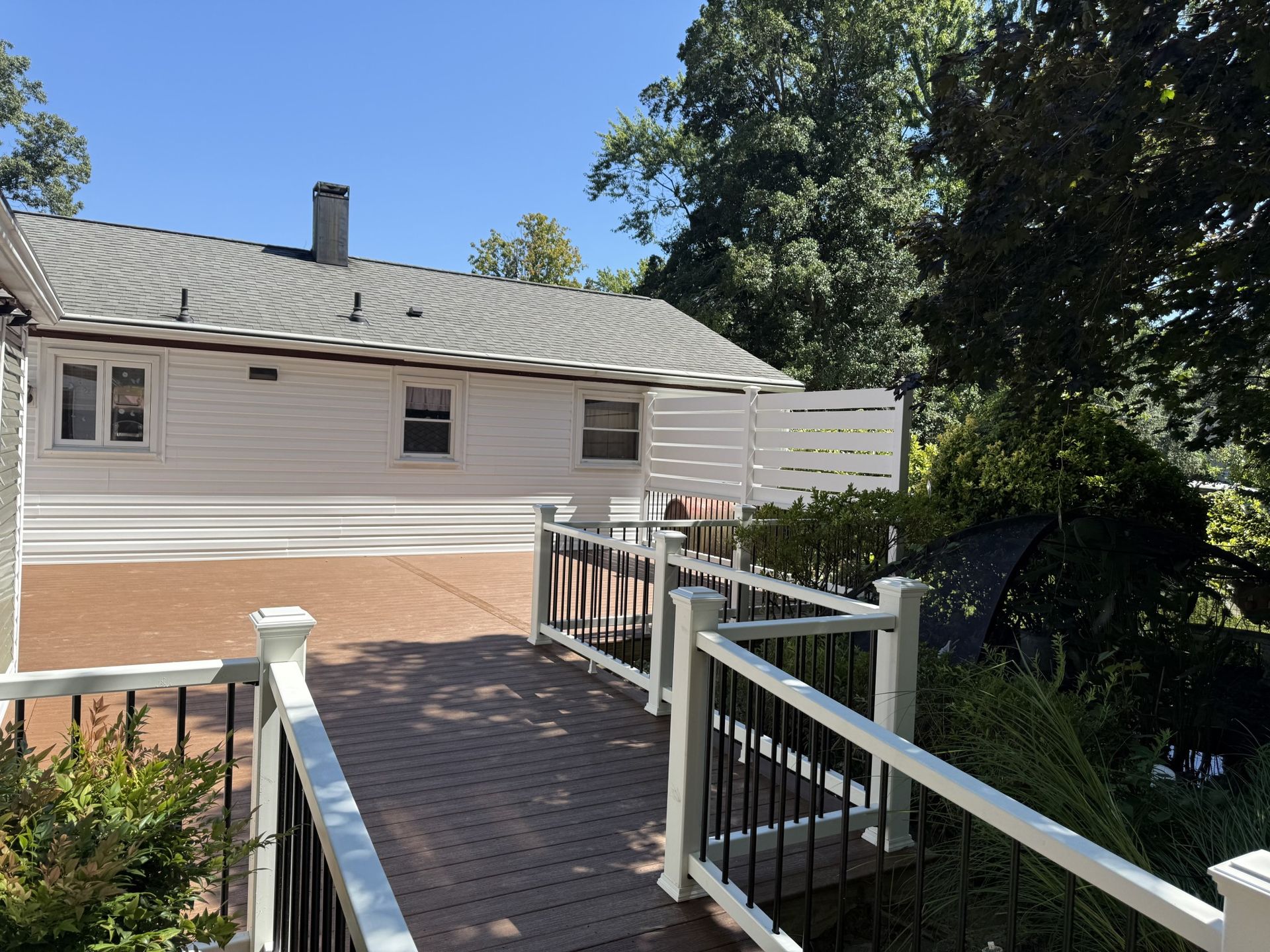 Backyard deck with white railing, brown deck, and white house on a sunny day.
