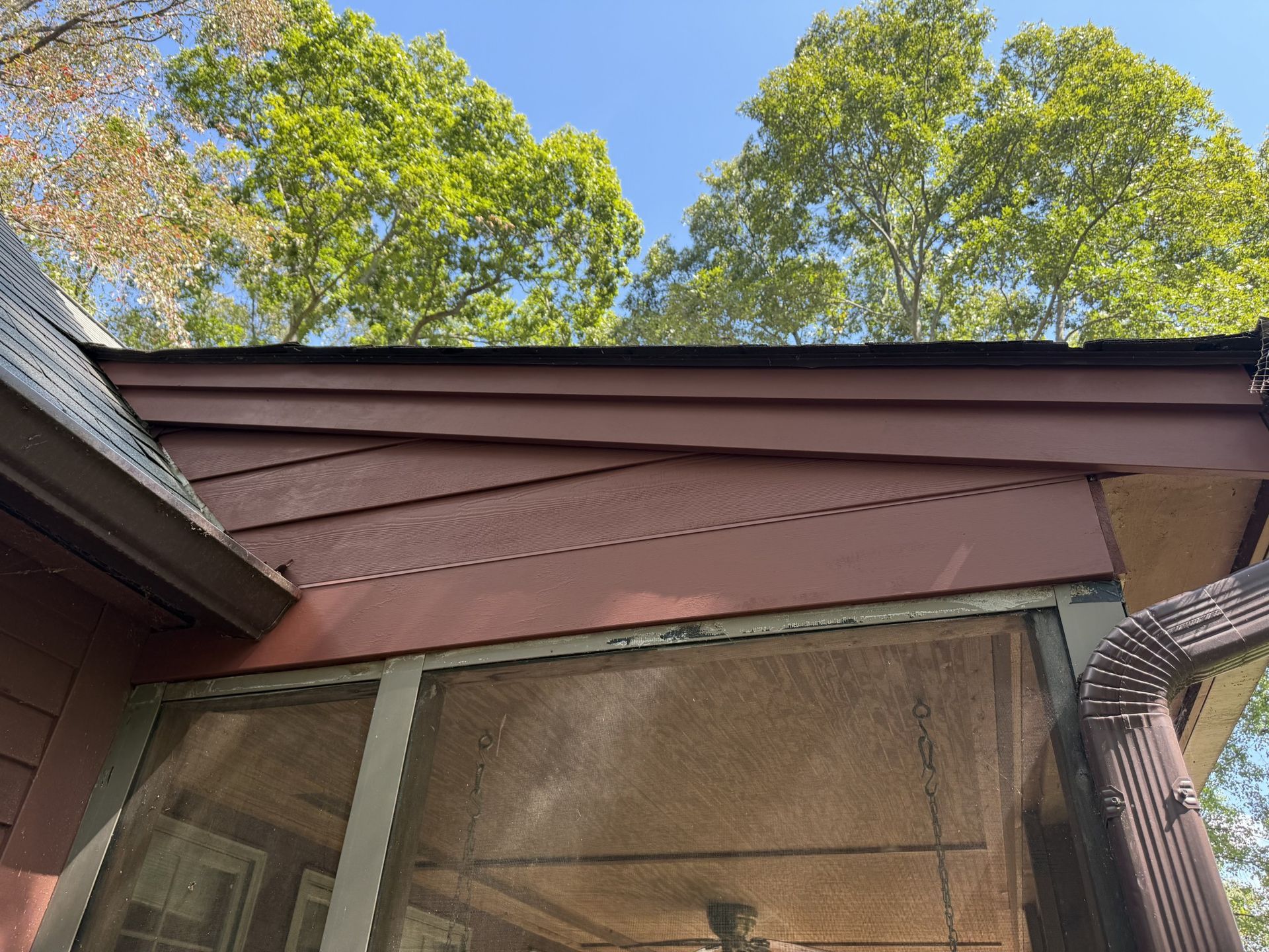 Red siding and roof with screen porch and trees in background.