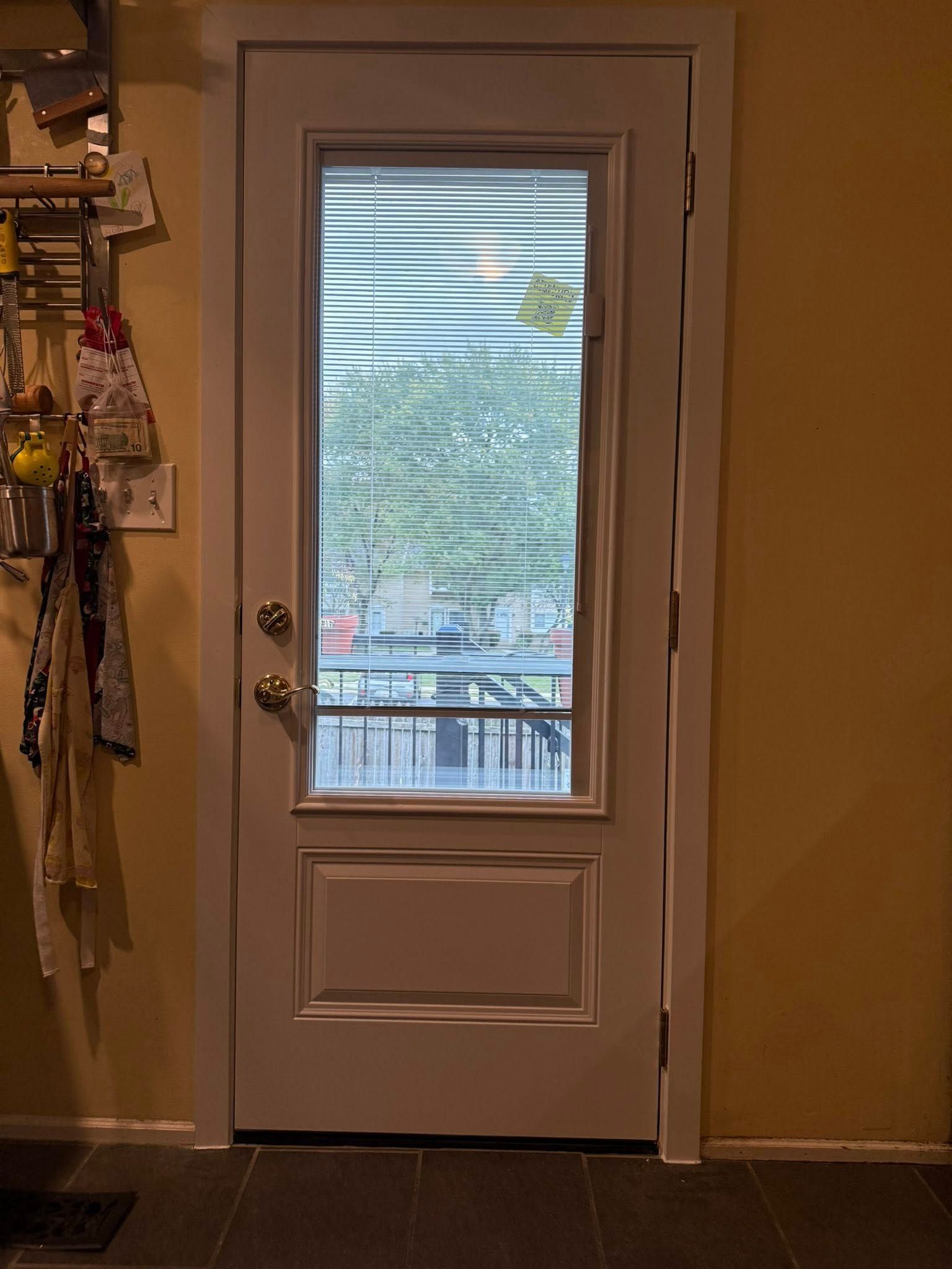 White door with glass pane, leading outside. Light reflects on the window. Interior is yellow with black tile floor.