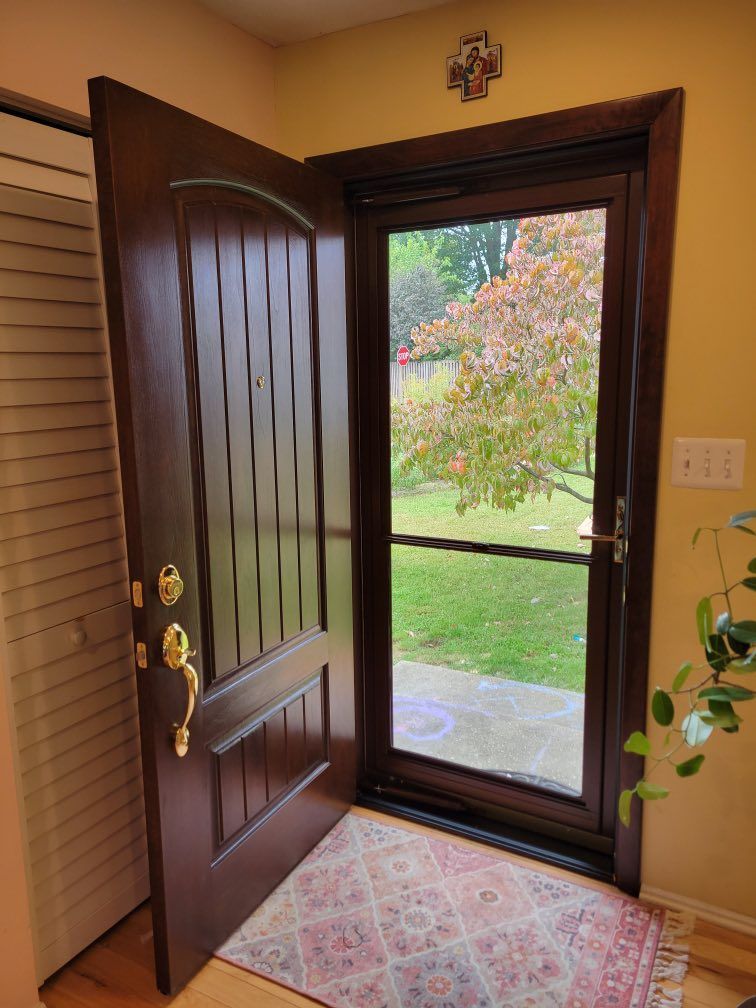 Brown wooden front door open to a green yard with a red patterned rug.