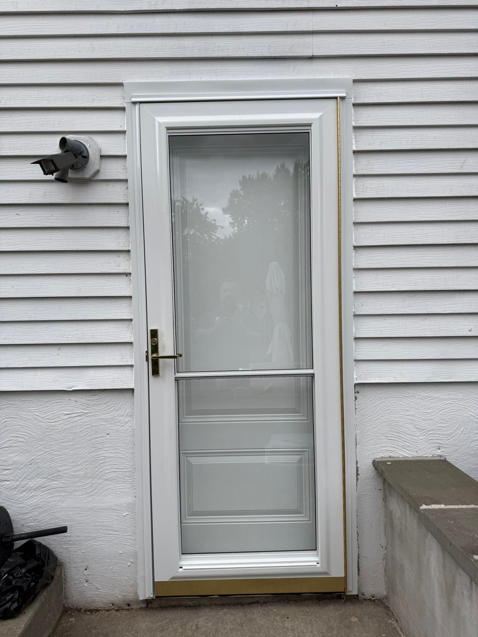 White screen door on a light gray house. The door is slightly ajar.