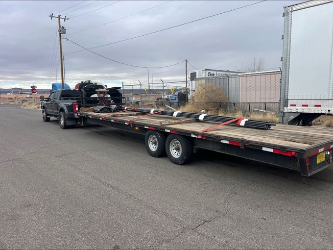 Flatbed trailer carrying equipment parked on a roadside under overcast skies