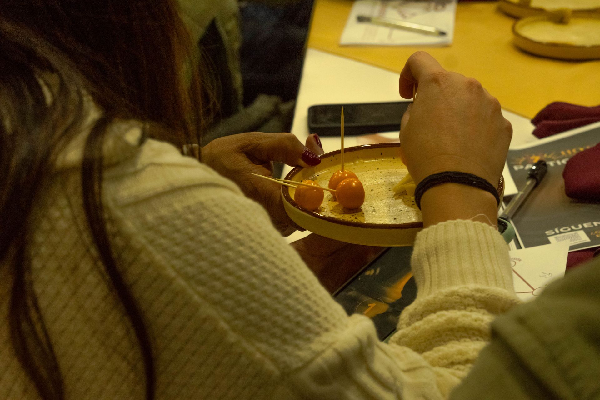 Person holding a small plate with three orange, round foods.  Table setting.
