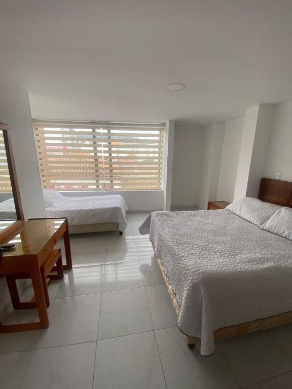 Hotel room with a double bed, single bed, desk, and window with blinds.