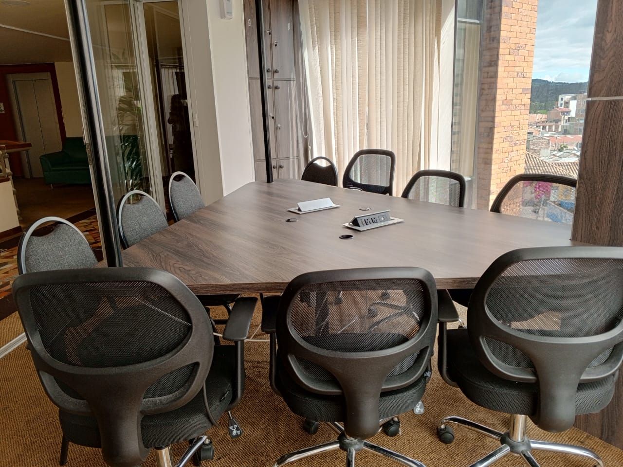 Meeting room with large table and mesh-back chairs. Balcony view with curtains.