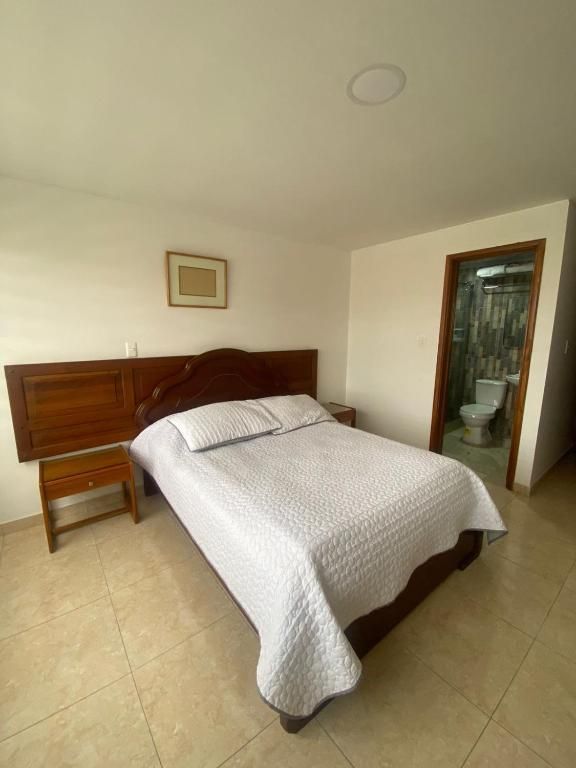 Bedroom with bed, nightstand, door to bathroom. Light colored walls and floors.