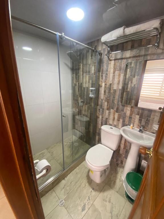 Bathroom with a glass shower, toilet, sink, and towel rack. The walls are a mix of white and brown tiles.