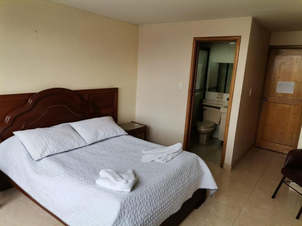 Hotel room with a bed, bathroom door, and wooden door. Neutral color walls and tile flooring.