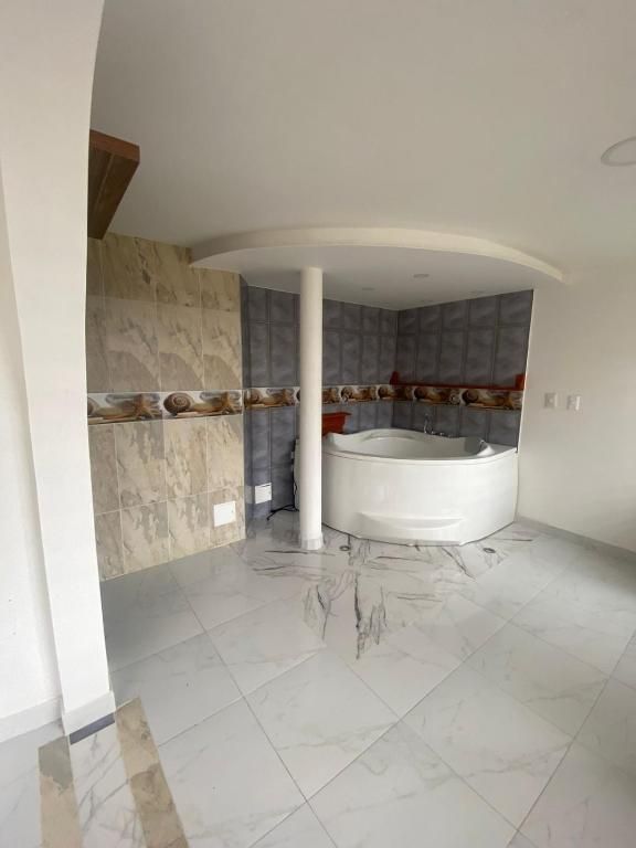 Bathroom with a white circular jacuzzi, column support, marble-like tiles on the walls and floor.