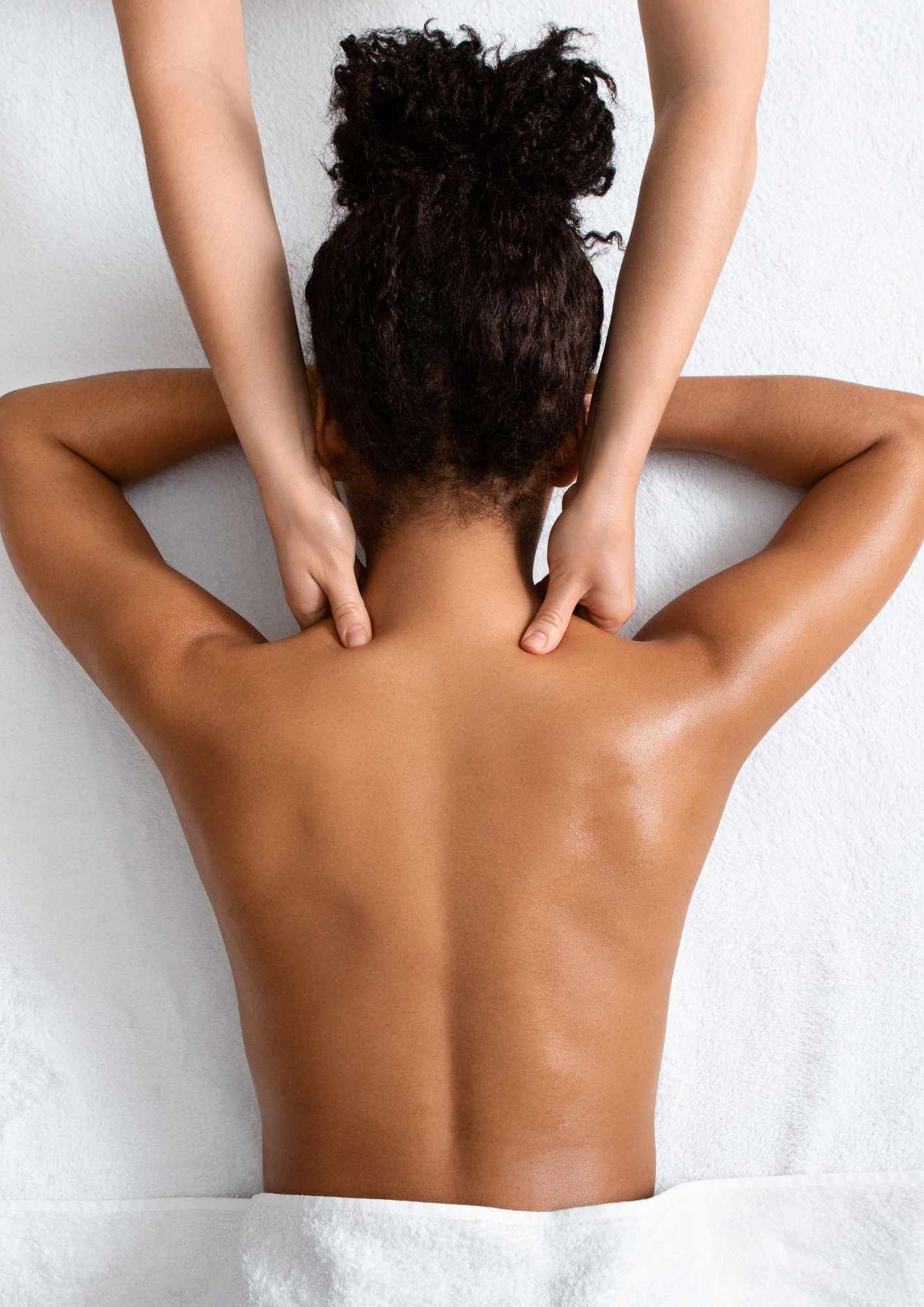 A woman receives a massage; hands on shoulders, back on white towel.