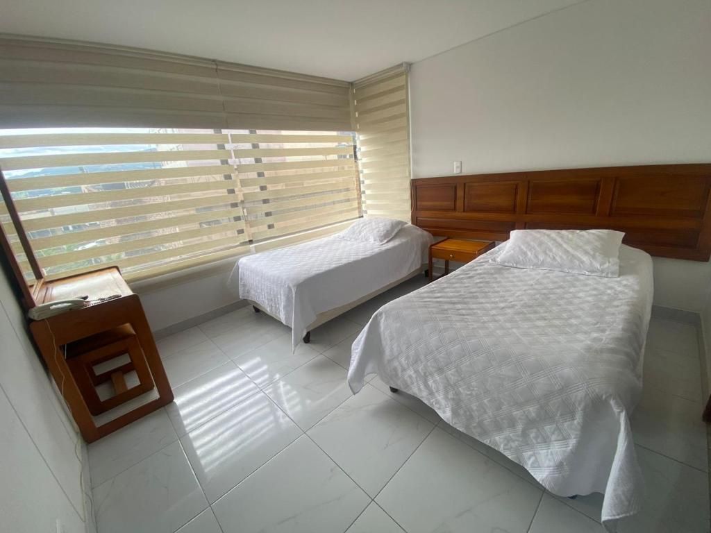 Two twin beds with white linens in a bright room with a window and a wooden desk.
