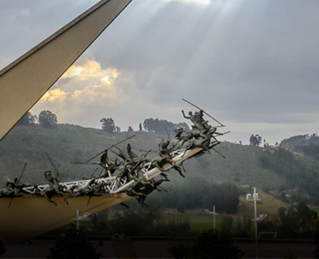 Sculpture of flying horses and riders on the roof of a building, with a hilly landscape in the background.