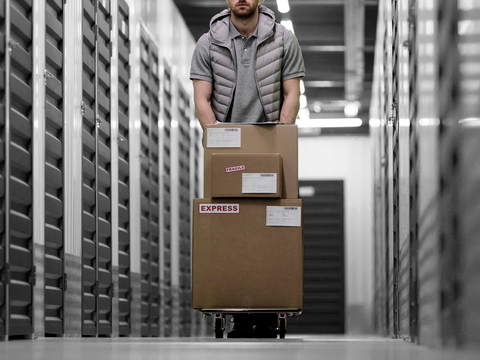 A man is pushing a cart filled with boxes in a warehouse.