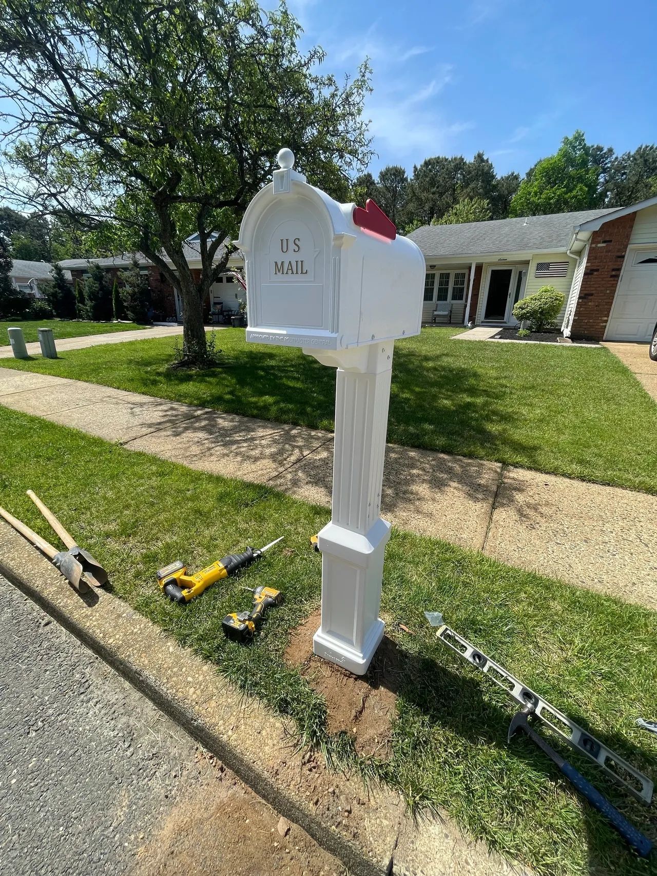 A white mailbox is sitting on the side of the road in front of a house.