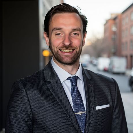 Man in suit smiles outdoors with city background.