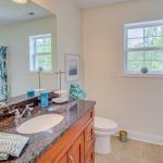 A bathroom with a sink , toilet , mirror and window.