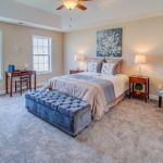 A bedroom with a bed , ottoman , desk and chairs.