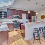 A kitchen with wooden cabinets , stools , a stove , microwave and refrigerator.