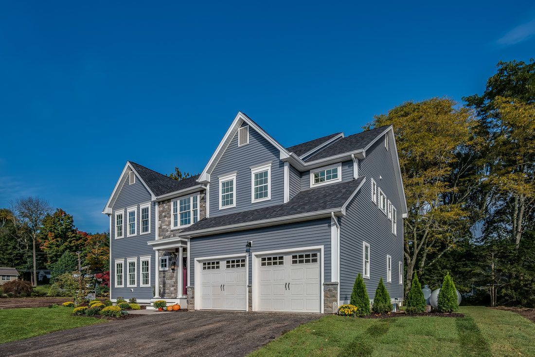 A large gray house with two garages is sitting on top of a lush green hillside.