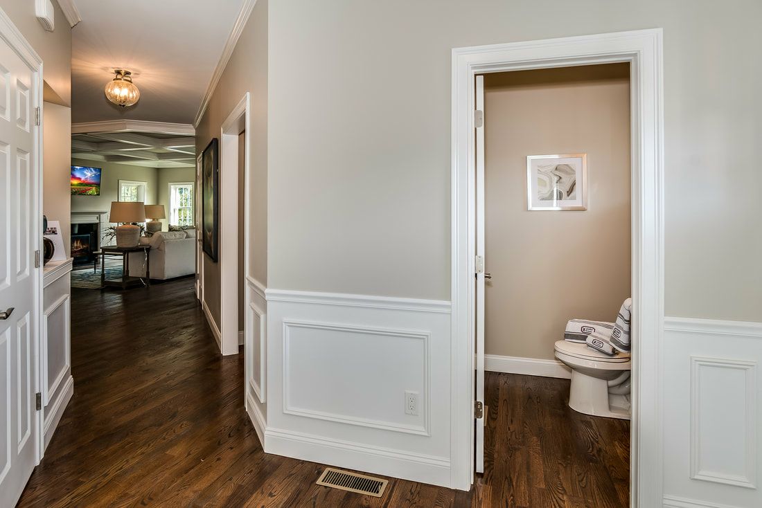 A hallway with hardwood floors and a toilet in a house.