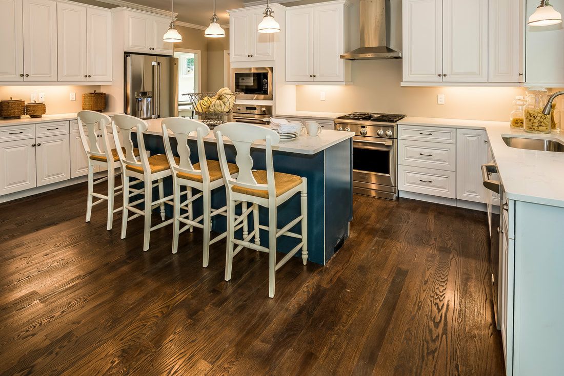 A kitchen with white cabinets , hardwood floors , and a large island.