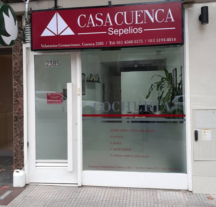 Exterior de la funeraria Casa Cuenca Sepelios con puerta de vidrio, dirección 2385 y señalización roja.