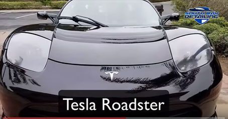 A black tesla roadster is parked on the side of the road.
