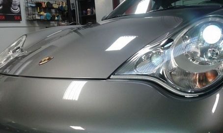 A close up of a car 's headlight and hood in a garage.