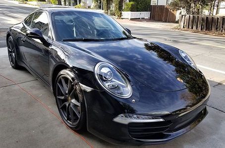 A black porsche 911 is parked on the side of the road.