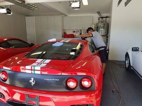 A man is cleaning a red sports car in a garage.