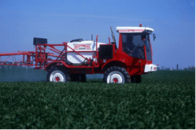 a red and white tractor is spraying a field of grass .