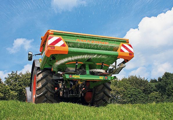 a green and orange tractor is spraying water on a lush green field .