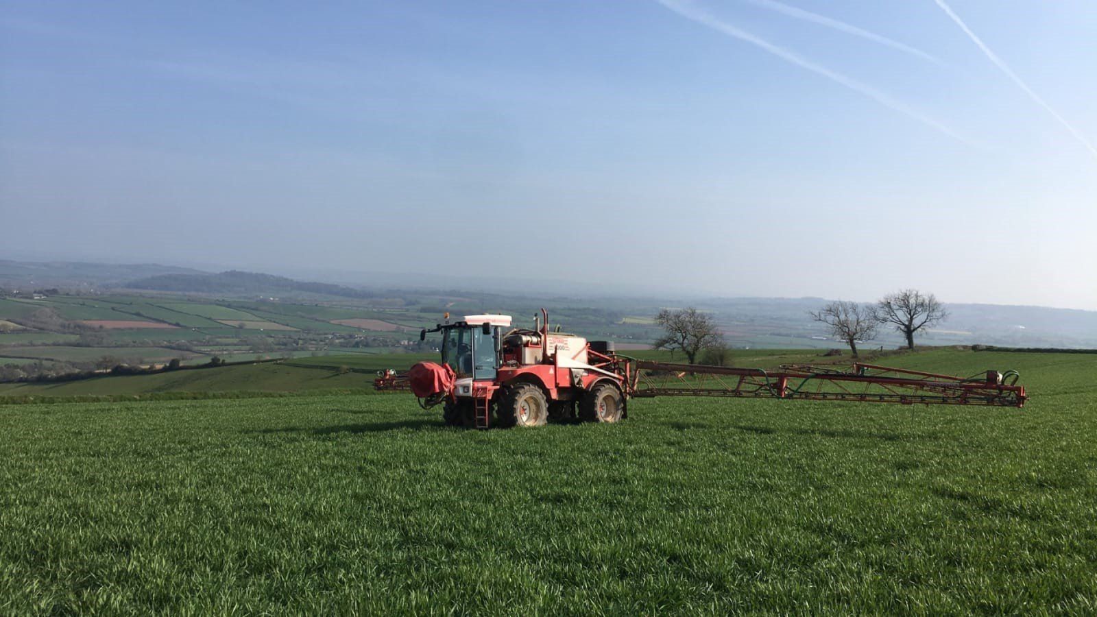 a red and white tractor is spraying a green field