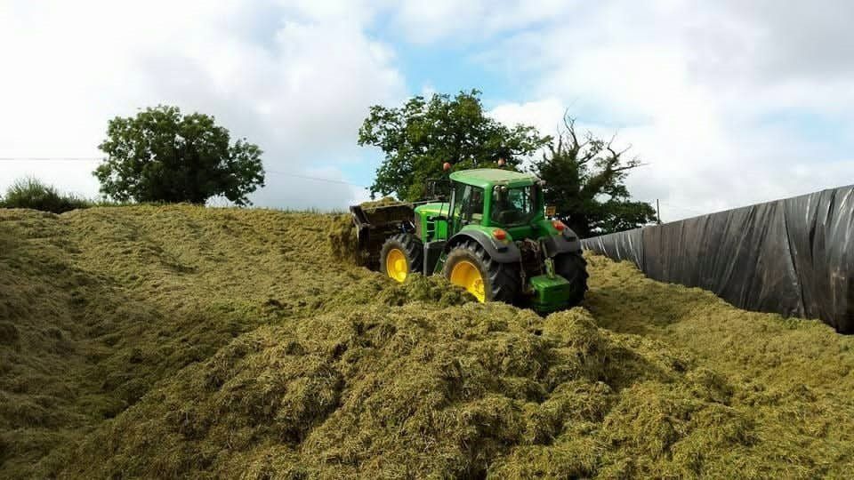 a green tractor is driving through a pile of hay .