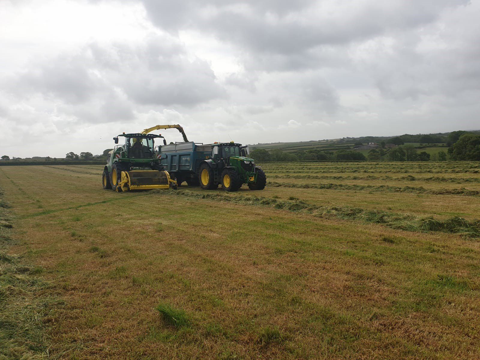 two john deere tractors are working in a field