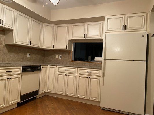 A kitchen with white cabinets , a refrigerator , a dishwasher , and a window.